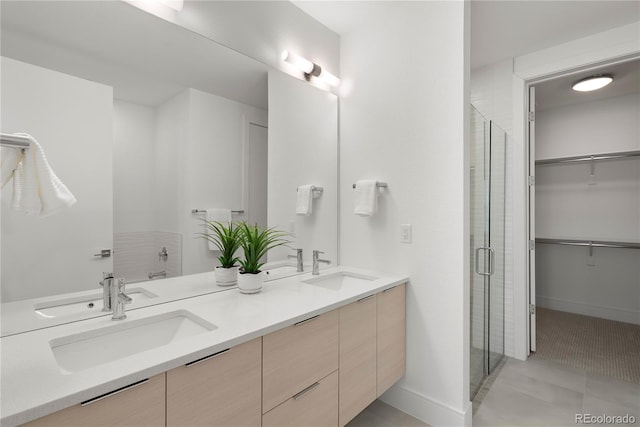 full bath featuring double vanity, a spacious closet, a shower stall, and a sink