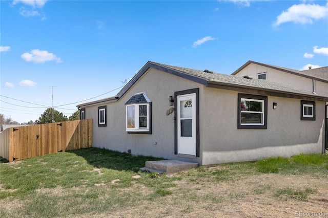 rear view of property featuring a yard, a shingled roof, stucco siding, and fence