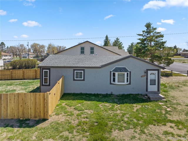 view of side of home with a yard, fence, a shingled roof, and stucco siding
