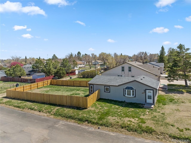 view of property exterior with a shingled roof, stucco siding, a residential view, and a fenced backyard