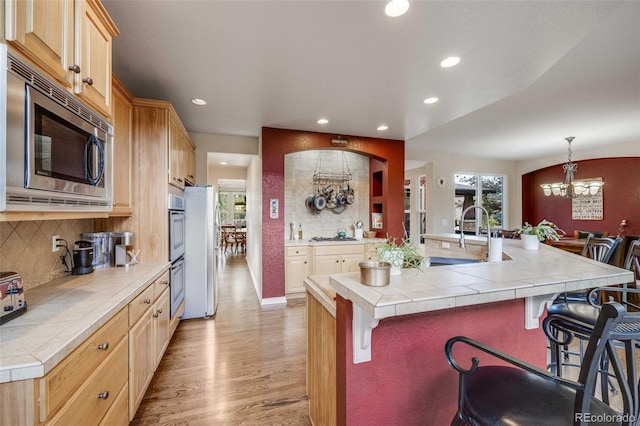 13324 W 86th Dr, Arvada, CO 80005 - kitchen with stainless steel appliances, a chandelier, a sink, a breakfast bar area, and light wood-style floors