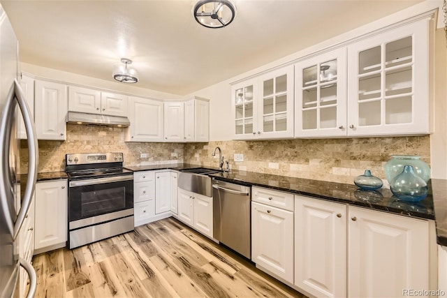 kitchen with appliances with stainless steel finishes, white cabinetry, dark stone counters, and sink