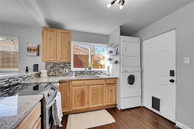 kitchen with light brown cabinetry, sink, stainless steel range with electric stovetop, stacked washer / drying machine, and light stone countertops