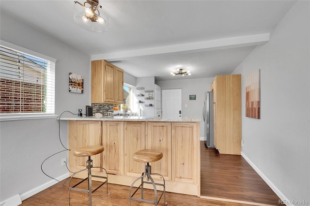 kitchen featuring light brown cabinetry, dark hardwood / wood-style floors, stainless steel fridge, kitchen peninsula, and light stone countertops