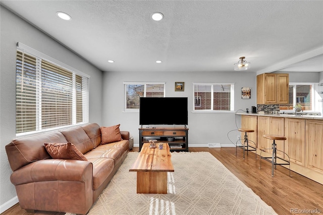 living room featuring sink, light hardwood / wood-style flooring, and a textured ceiling