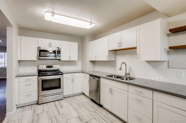 kitchen featuring stainless steel appliances, a sink, white cabinetry, open shelves, and tasteful backsplash