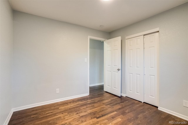 unfurnished bedroom with a closet, baseboards, and dark wood-style flooring