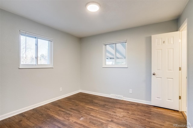 unfurnished room with dark wood-style flooring, visible vents, and baseboards