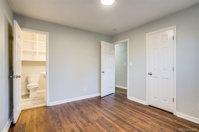 unfurnished bedroom with ensuite bathroom, dark wood-style flooring, and baseboards