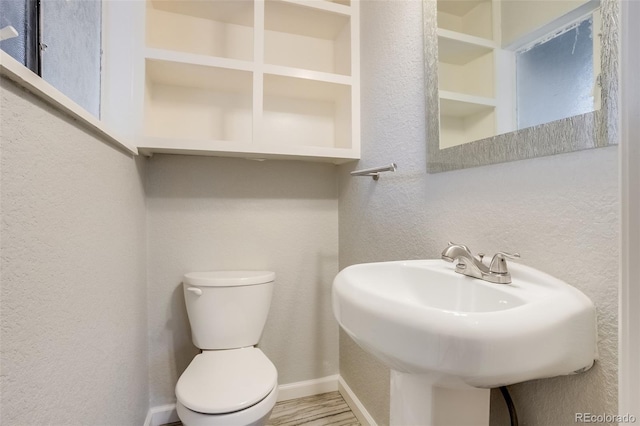 bathroom featuring a textured wall, toilet, wood finished floors, a sink, and baseboards