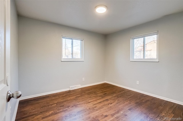 empty room with a wealth of natural light, dark wood finished floors, visible vents, and baseboards