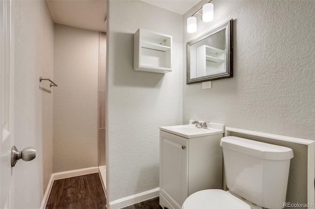 bathroom with a textured wall, toilet, wood finished floors, vanity, and baseboards