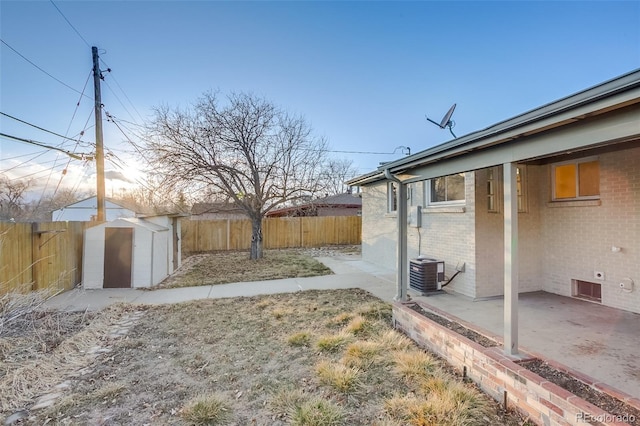 view of yard with a fenced backyard, an outbuilding, a patio area, a shed, and central AC