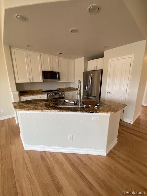 kitchen with sink, white cabinetry, dark stone counters, stainless steel appliances, and light hardwood / wood-style floors