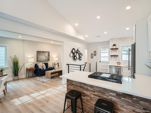 kitchen with a peninsula, stainless steel appliances, vaulted ceiling, white cabinets, and light wood-style floors