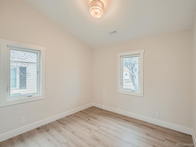 empty room featuring light wood finished floors, visible vents, baseboards, and lofted ceiling