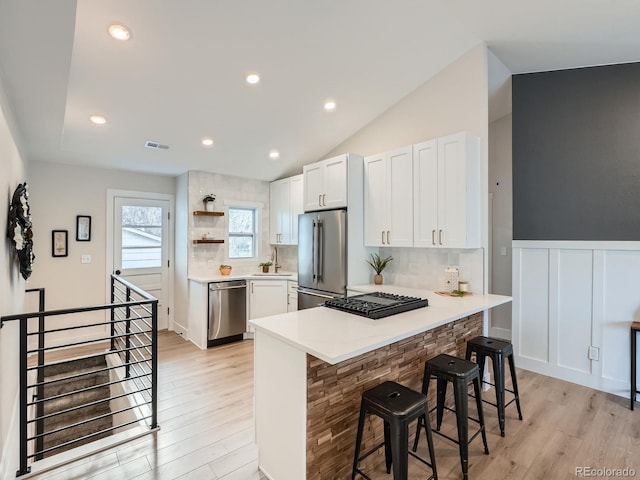 kitchen with visible vents, a breakfast bar, a peninsula, stainless steel appliances, and open shelves