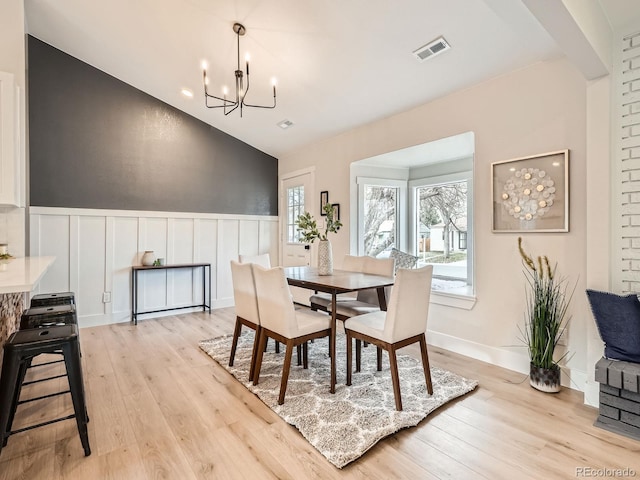 dining area featuring a wainscoted wall, visible vents, lofted ceiling, a notable chandelier, and light wood-type flooring