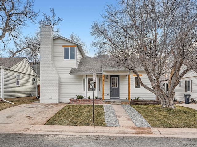 view of front facade with a porch, a chimney, a front yard, and a shingled roof