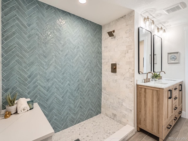 full bath with a sink, visible vents, tiled shower, and double vanity