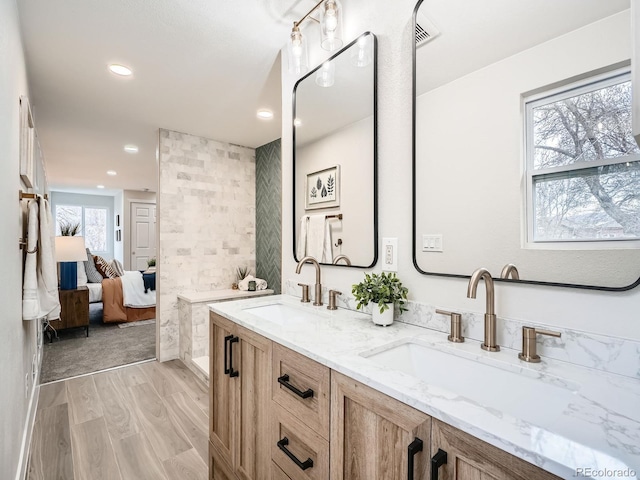 ensuite bathroom featuring a sink, connected bathroom, wood finished floors, and double vanity