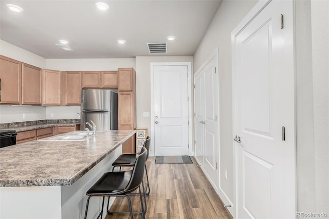 kitchen featuring sink, a breakfast bar area, stainless steel fridge, light hardwood / wood-style floors, and a center island with sink