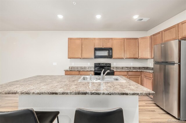 kitchen with sink, a breakfast bar area, black appliances, and a center island with sink