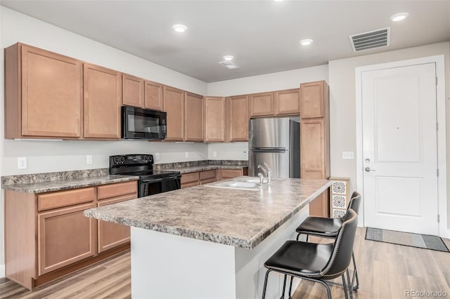 kitchen featuring light wood-type flooring, sink, a center island with sink, and black appliances