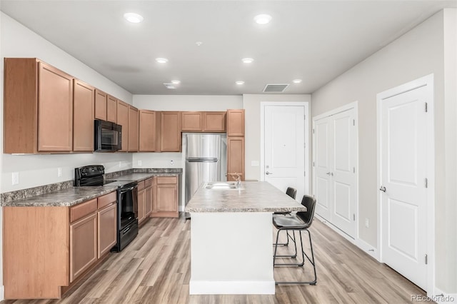 kitchen featuring sink, a breakfast bar, a kitchen island with sink, light hardwood / wood-style floors, and black appliances