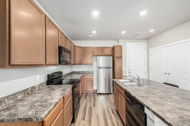 kitchen featuring an island with sink, sink, light hardwood / wood-style flooring, and black appliances