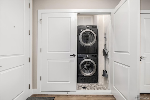 washroom with hardwood / wood-style flooring and stacked washer and clothes dryer