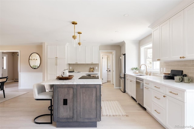 kitchen featuring white cabinetry, sink, stainless steel appliances, decorative light fixtures, and a kitchen island