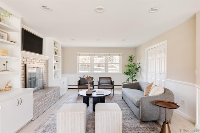 living room featuring a fireplace, light wood-type flooring, and a baseboard heating unit