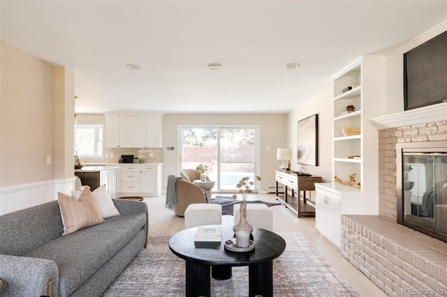 living room with a wealth of natural light, light hardwood / wood-style flooring, and a brick fireplace