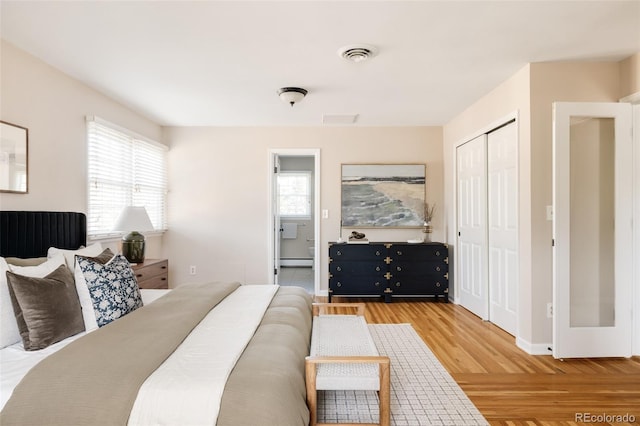 bedroom with a baseboard heating unit, multiple windows, a closet, and light hardwood / wood-style flooring