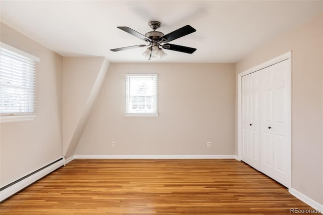 unfurnished bedroom with ceiling fan, a closet, baseboard heating, and light hardwood / wood-style flooring