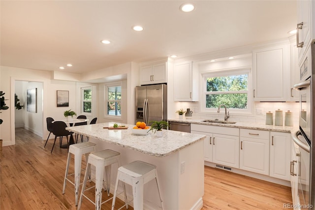 kitchen with a center island, sink, light hardwood / wood-style flooring, appliances with stainless steel finishes, and white cabinetry