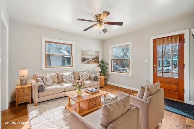 living area featuring light wood-style floors, ceiling fan, baseboards, and a wealth of natural light