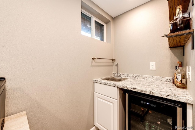 bar with light stone counters, white cabinets, wine cooler, and sink