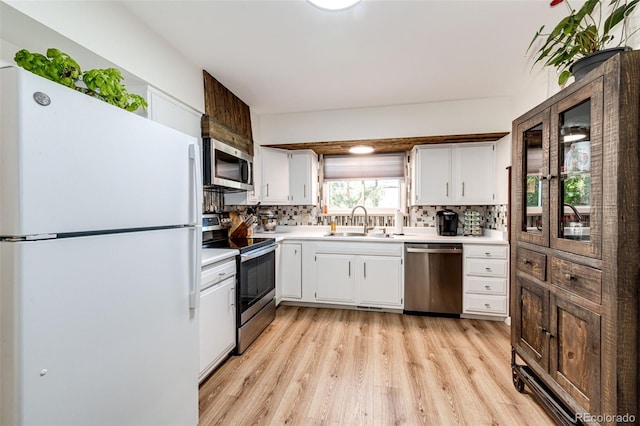 kitchen featuring light wood-type flooring, sink, white cabinetry, backsplash, and appliances with stainless steel finishes