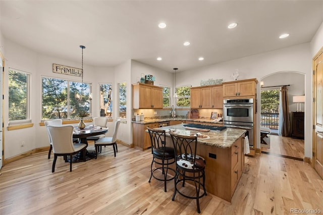 kitchen with arched walkways, light wood-style flooring, a center island, a sink, and recessed lighting