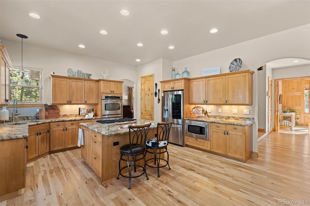 kitchen with arched walkways, a center island, tasteful backsplash, appliances with stainless steel finishes, and a sink