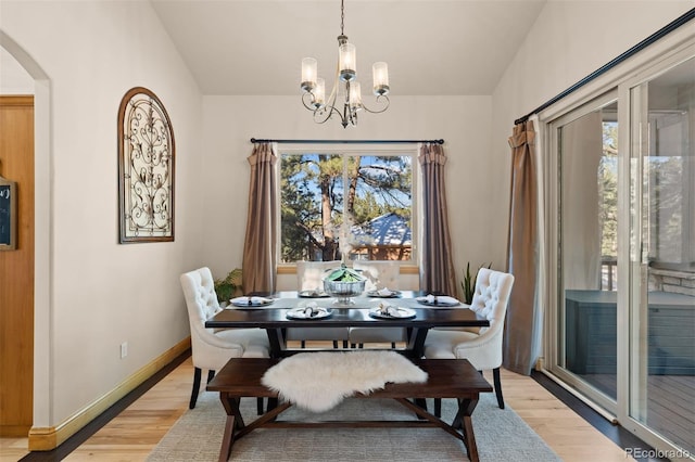 dining room with arched walkways, light wood-type flooring, baseboards, and a notable chandelier