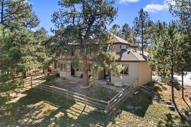 rear view of house featuring roof with shingles, a patio area, fence, and stucco siding