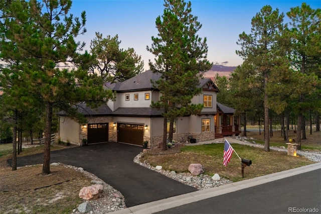 view of front of property featuring aphalt driveway, stone siding, a garage, and stucco siding