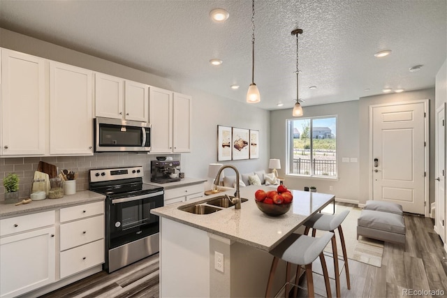 kitchen with pendant lighting, an island with sink, sink, white cabinets, and stainless steel appliances