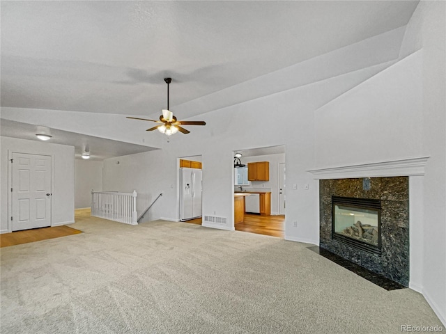 unfurnished living room featuring vaulted ceiling, light colored carpet, a premium fireplace, and ceiling fan