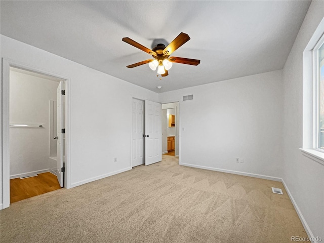 unfurnished bedroom featuring ceiling fan, ensuite bath, and light carpet