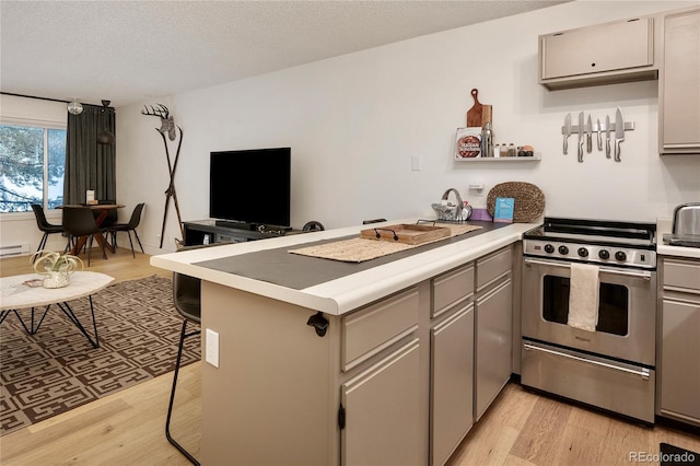 kitchen with gray cabinetry, stainless steel stove, light hardwood / wood-style floors, a kitchen bar, and kitchen peninsula