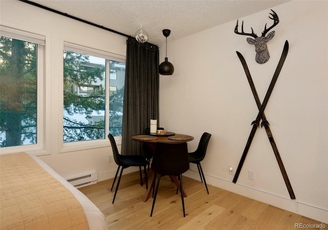 dining space featuring plenty of natural light, light hardwood / wood-style floors, a textured ceiling, and a baseboard heating unit